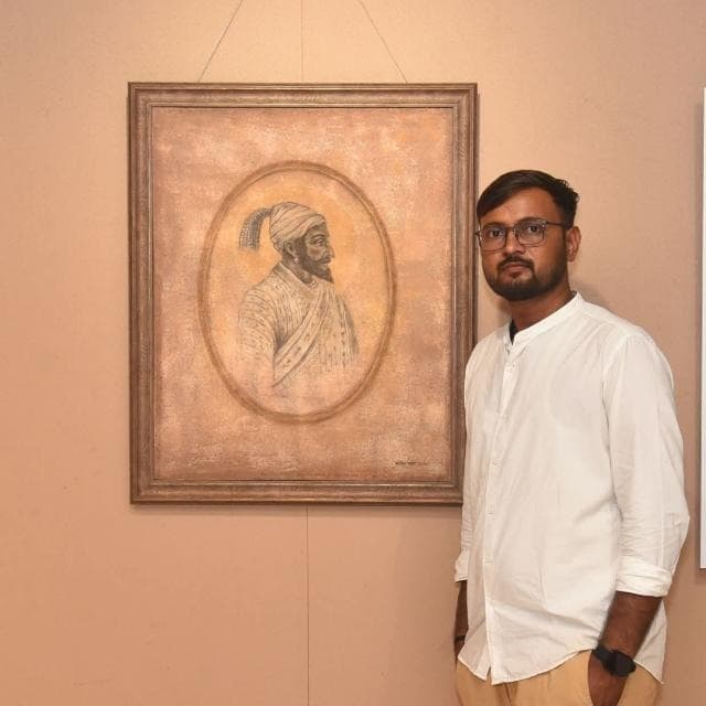 Manoj Kisan Pawar standing beside a framed portrait painting of Chhatrapati Shivaji Maharaj at an art exhibition