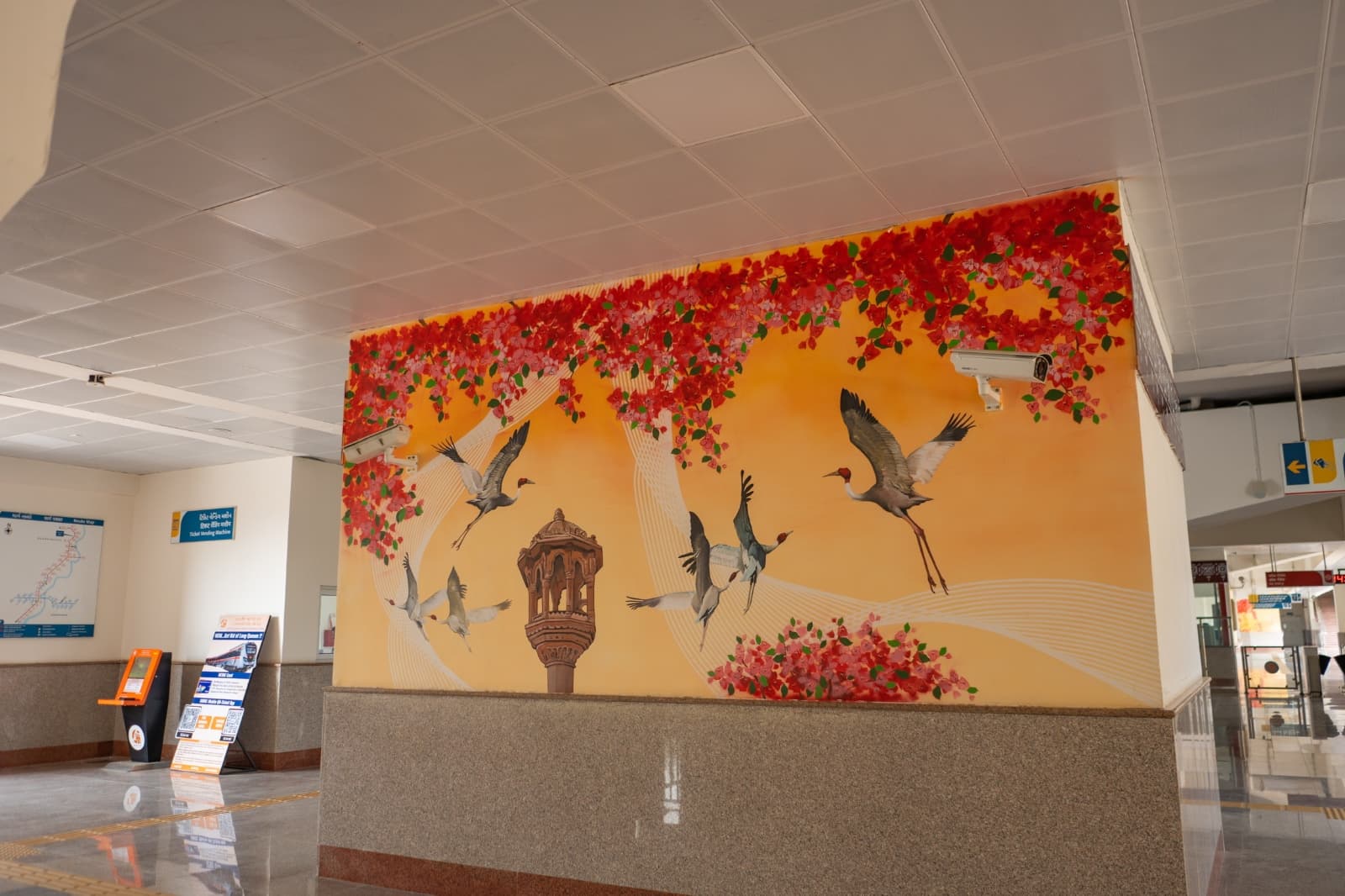 Indoor mural of flying cranes beneath red bougainvillea flowers at a metro station concourse