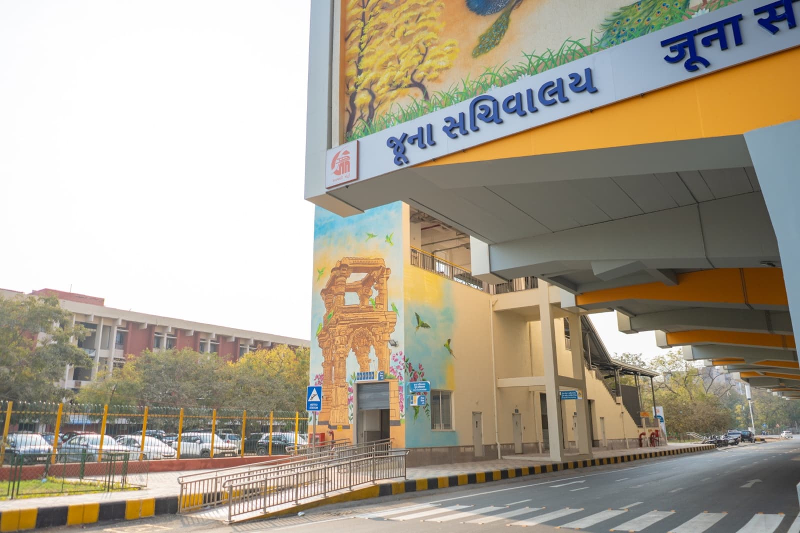 Station entrance pillar mural of a heritage stepwell arch with parrots at Juna Sachivalaya metro station
