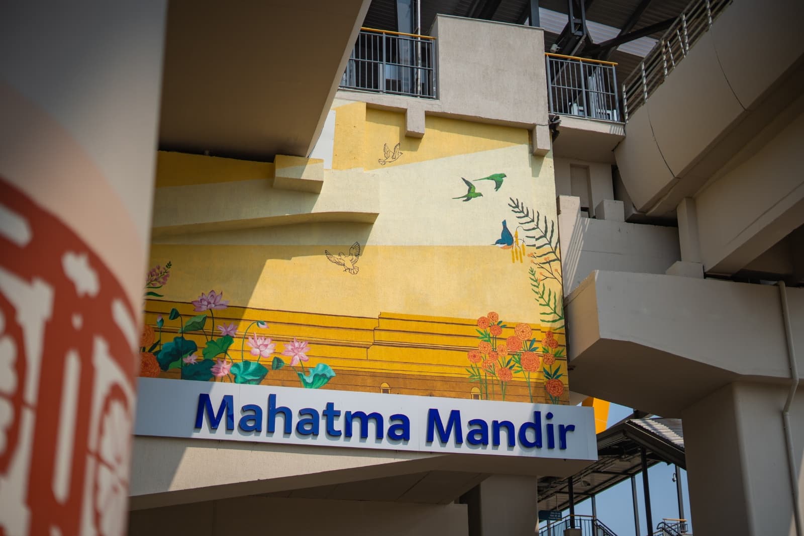 Hand-painted mural of lotus flowers, marigolds and birds above the Mahatma Mandir metro station signage