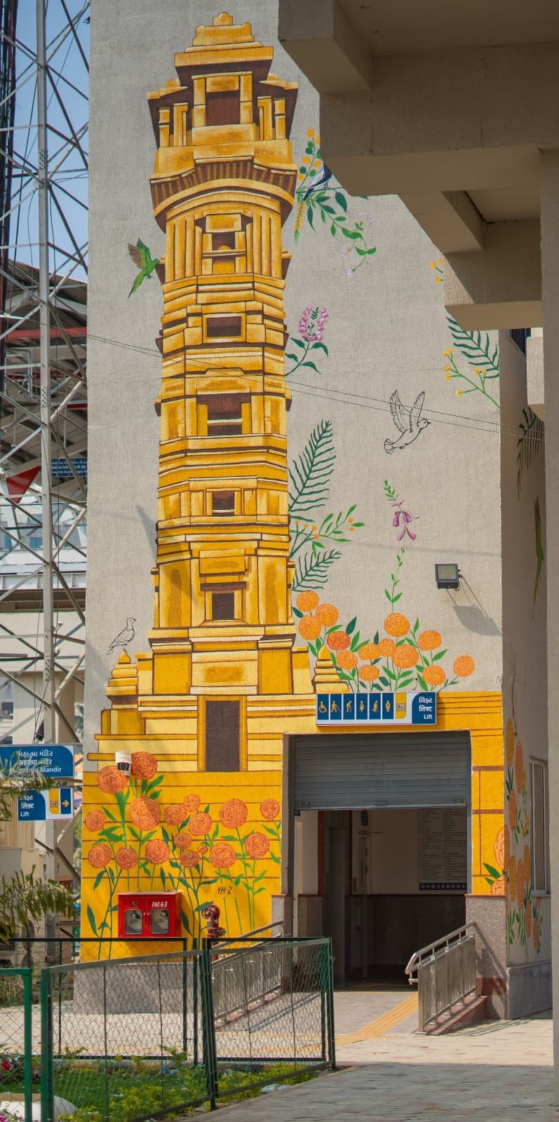 Tall decorative mural of a temple tower with birds and marigold flowers at Mahatma Mandir metro station entrance
