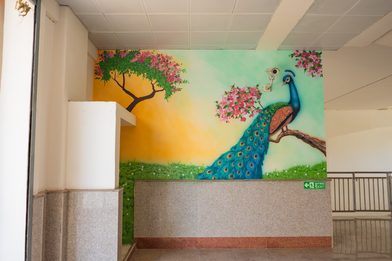 Indoor mural of a peacock perched on a blossom branch at a metro station concourse