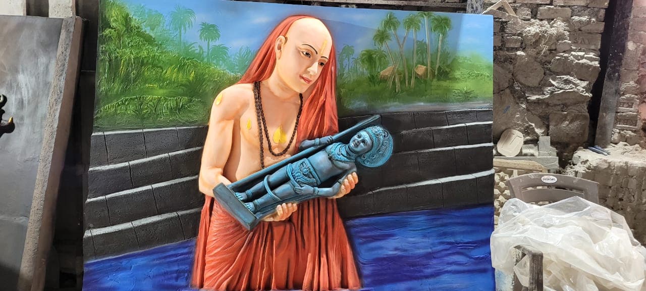 Hand-painted FRP relief panel of an acharya carrying a deity through water, riverside palm trees in the background